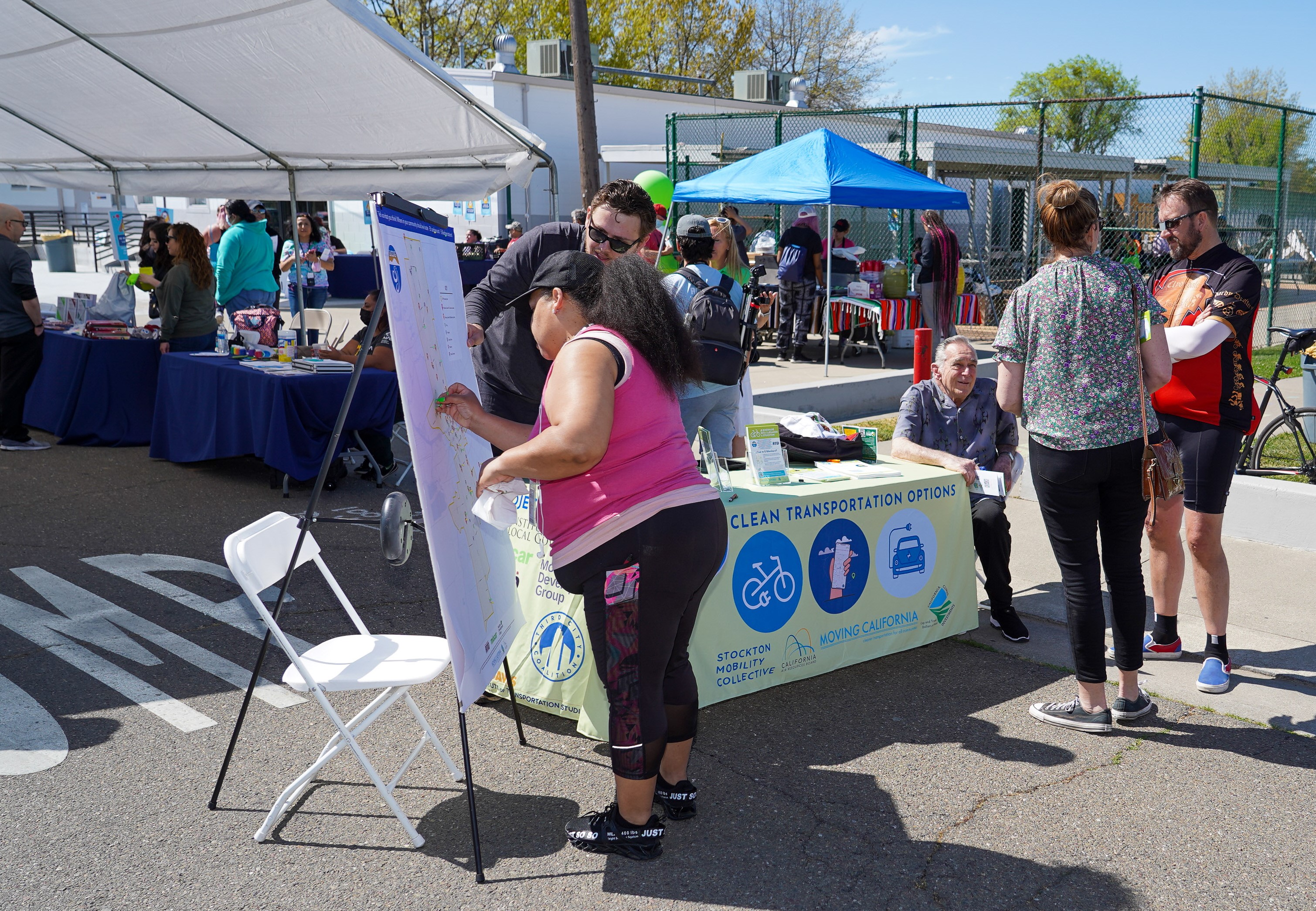 Community members at an outdoor San Joaquin Council of Governments engagement event, marking a regional map beside a Clean Transportation Options information table.